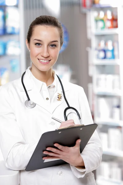 で薬局。若い女性の笑みを浮かべて薬剤師 stethosco を着ています。 — ストック写真