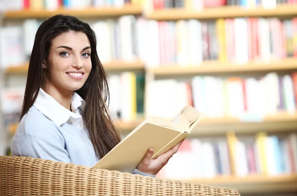 Улыбающаяся студентка с книгой в руках, сидящая в кресле в — стоковое фото
