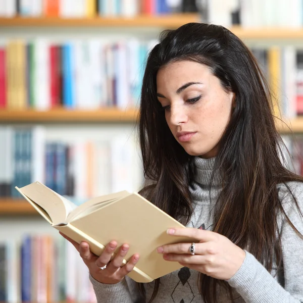 Estudante do sexo feminino lendo um livro na biblioteca — Fotografia de Stock