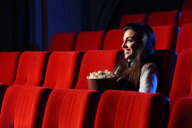 A pretty young woman sitting in an empty theater, she eats popco clipart