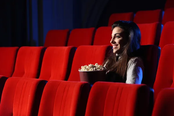 Гарненька молода жінка сидить у порожньому театрі, вона їсть попко — стокове фото