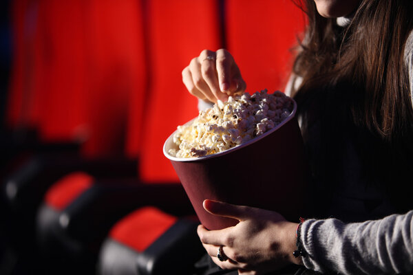 Крупным планом руки девушки в кинотеатре, она ест поп
