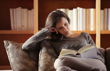 Portrait of a young woman lying on couch with book clipart