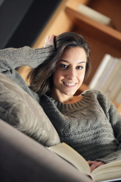 Портрет счастливой молодой женщины, лежащей на диване с книгой — стоковое фото