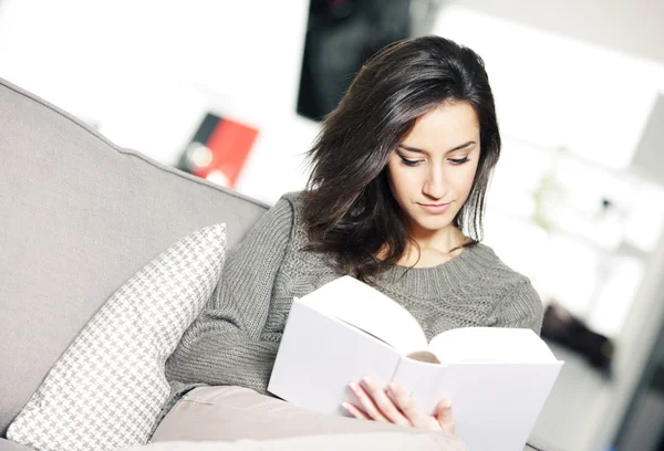 Portrait of a young woman lying on couch with book — Stock Photo, Image