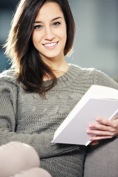 Porträt einer glücklichen jungen Frau, die mit Buch auf der Couch liegt — Stockfoto