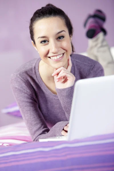 Genç kadın yatakta laptop kullanırken rahat bir portresi — Stok fotoğraf