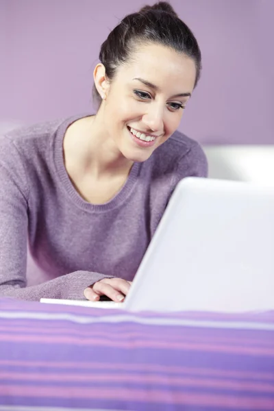 Portrait of a young female relaxing in bed while using laptop — Stock Photo, Image