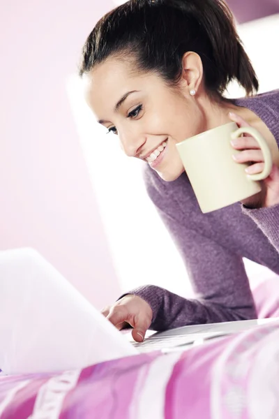 Happy casual young lady using laptop while lying in bed — Stock Photo, Image
