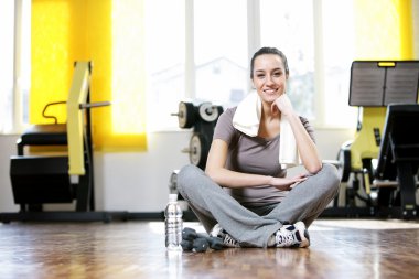 Young woman sitting on the gym's floor after workout clipart