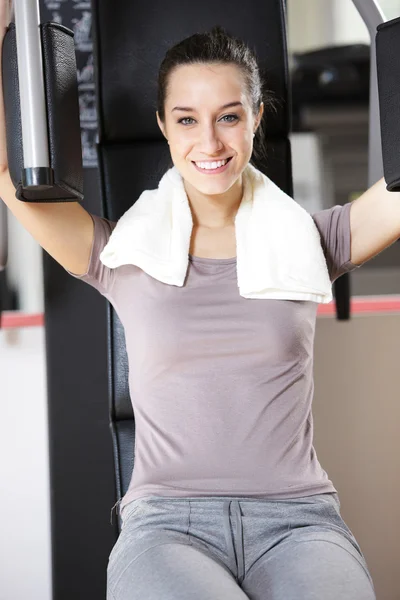 Mujer joven hace ejercicio en la máquina de entrenamiento con pesas — Foto de Stock