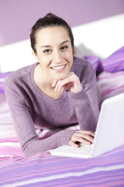 젊은 여성 편안한 침대에서 노트북을 사용 하는 동안의 초상화 — 스톡 사진