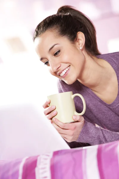Vacker flicka leenden på den bärbara datorn med en kopp kaffe i handen — Stockfoto