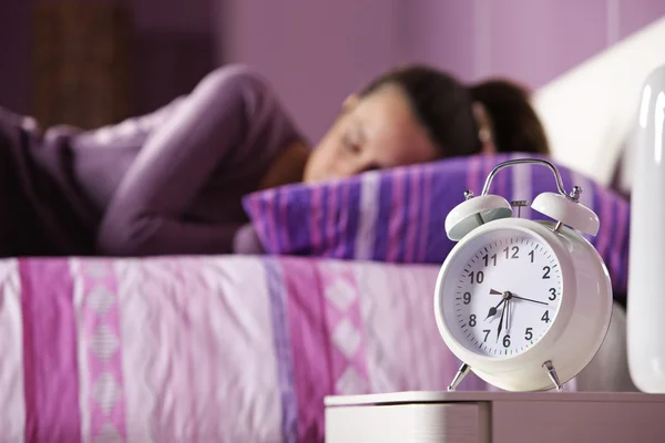 An alarm clock with a sleeping young woman in the background — Stock Photo, Image