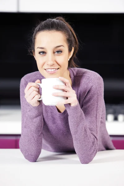 Mooie jonge vrouw met koffie terwijl in de keuken — Stockfoto