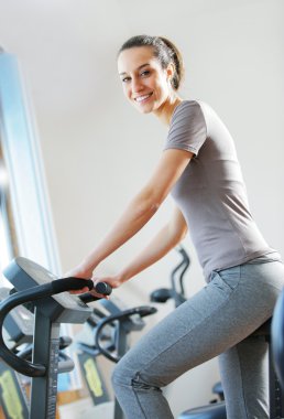 Portrait of young woman riding an exercise bike clipart