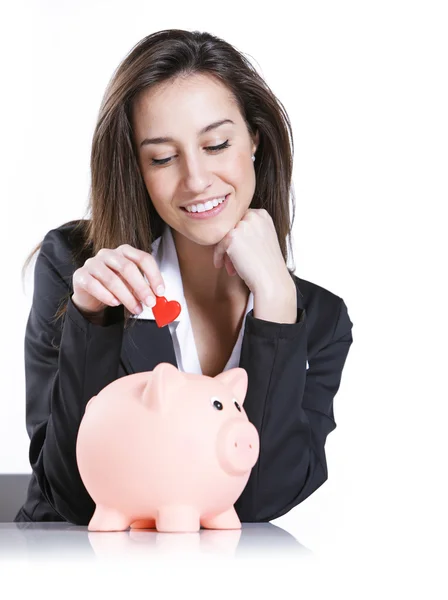 Close-up of young woman putting a red hearth into a piggy bank, — Stock Photo, Image