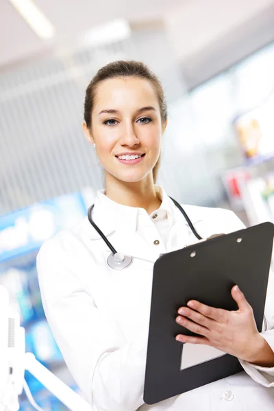 At pharmacy. A smiling young woman pharmacist wearing stethosco — Zdjęcie stockowe
