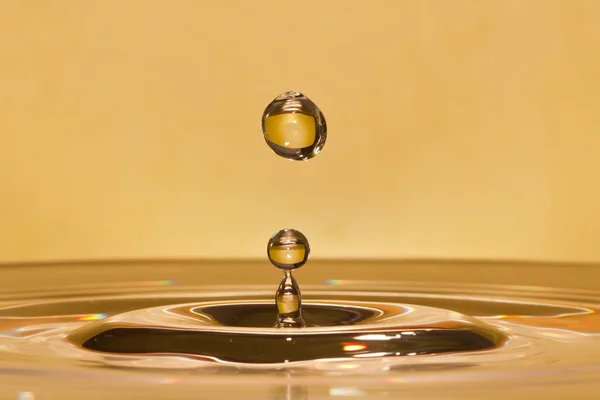 stock image Closeup of falling water-drop in a yellow liquid