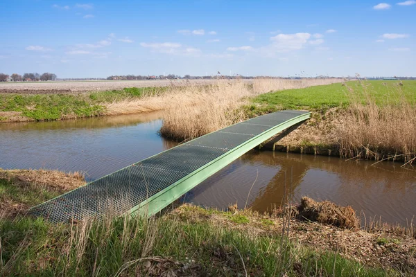 Landbouwgrond met voetgangers brug over een brede gracht — Stockfoto