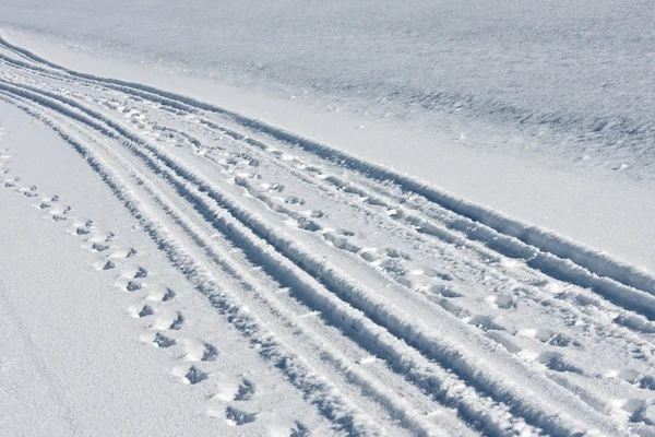 Hjulspår och fotspår i vit snö — Stockfoto