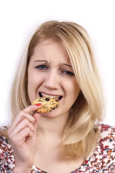 Young woman eating cookie with grimace — Stock Photo, Image