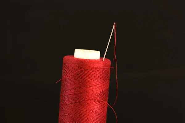 Nadel mit rotem Faden auf schwarzem Hintergrund — Stockfoto