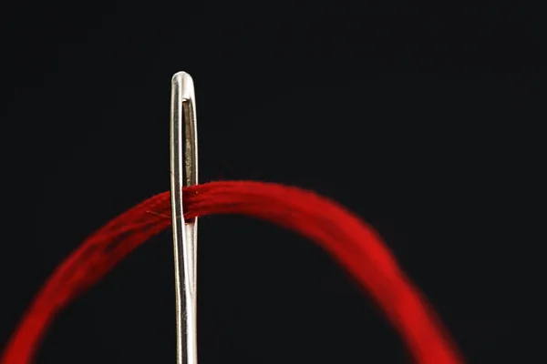Aiguille avec un fil rouge sur fond noir — Photo