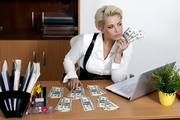Γυναίκα του ελκυστικού επιχειρηματικού κάθεται σε ένα τραπέζι και κρατώντας ένα dolla Φωτογραφία Αρχείου