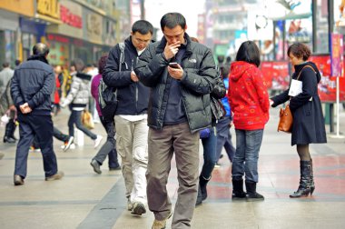 Two men using mobile phone on a busy pedestrian shopping street clipart