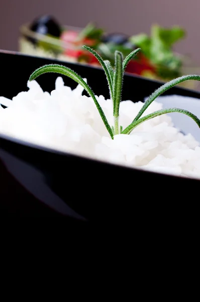 Rijst in zwarte kom op salade achtergrond — Stockfoto