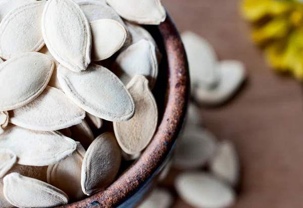 Ceramic bowl full of pumpkin seeds on wooden board — Stock Photo, Image