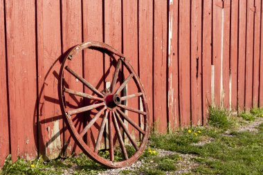 Old rustic wagon wheel beside a red barn. clipart