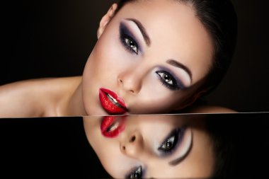 High fashion look.glamour fashion portrait of beautiful sexy brunette girl with bright makeup and red lips and her reflection in mirror table on dark clipart