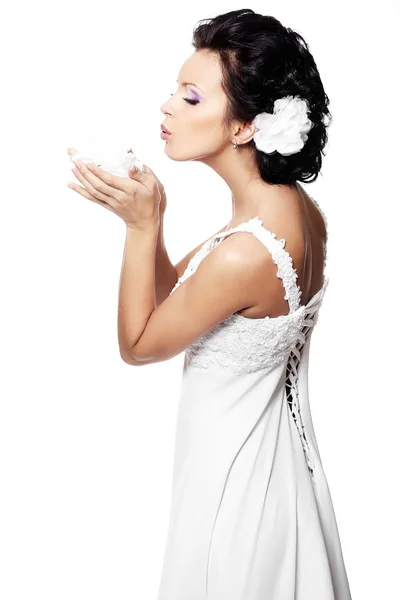 Joyeux sexy belle mariée fille brune en robe de mariée blanche avec fleur dans les mains avec coiffure et maquillage lumineux avec fleur dans les cheveux isolés sur blanc — Photo