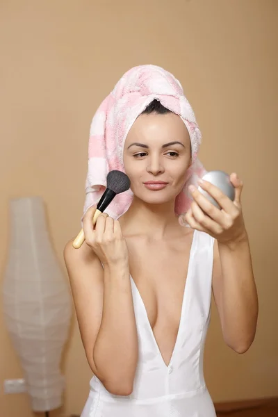 Mujer joven en toalla en la cabeza aplicando maquillaje en el espejo — Foto de Stock
