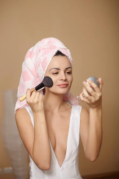 Krásná mladá žena v ručník na hlavě použití make-up v zrcadle — Stock fotografie