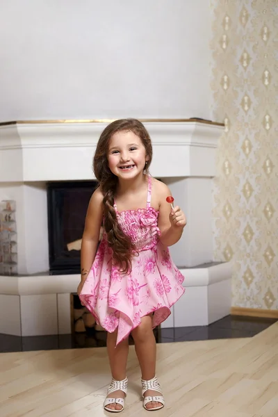 Schattige lachende meisje in roze jurk staande in de buurt van open haard thuis met — Stockfoto