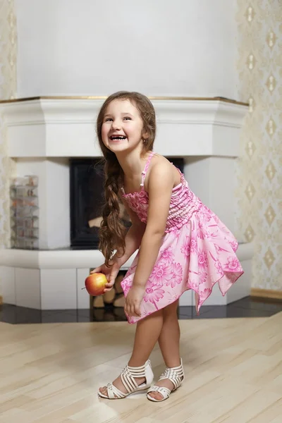 Schattige lachende meisje in roze jurk permanent in de buurt van open haard thuis apple — Stockfoto