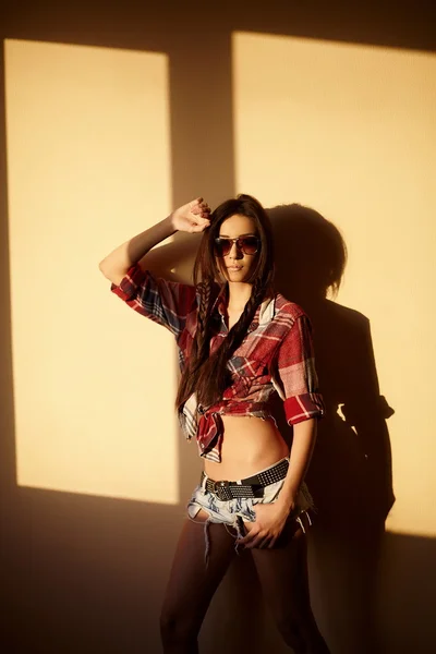 Портрет красивой моды сексуальная брюнетка в джинсах и красочная рубашка в очках за закатом в помещении — стоковое фото