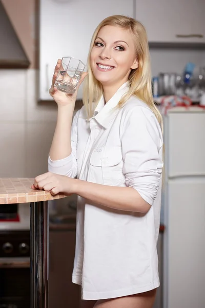 stock image Beautiful young woman holds a glass with water on kitchen