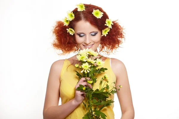 Πορτρέτο του όμορφη χαμογελαστό γυναίκα κοκκινομάλλα τζίντζερ σε κίτρινο ύφασμα με κίτρινο ροζ ζωηρόχρωμα λουλούδια στα μαλλιά που απομονώνονται σε λευκό κρατώντας λουλούδια — Φωτογραφία Αρχείου