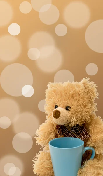 Teddy bear with a blue cup on a beige background — Stock Photo, Image