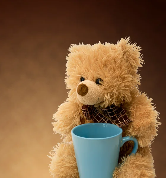 Urso de pelúcia com uma xícara azul em um fundo marrom — Fotografia de Stock