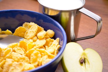 Corn flakes with milk and an apple on the table