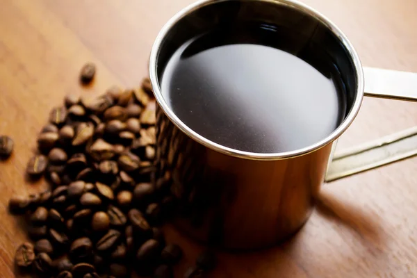 Egy csésze kávé és kávébab egy fa asztalon. — Stock Fotó