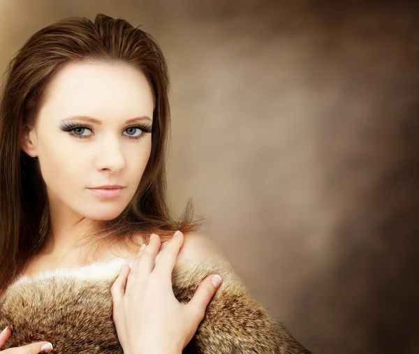 Schöne Frau in Pelzen auf braunem Hintergrund — Stockfoto