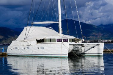 Sailing catamaran morred. Heavy sky background and reflections on water vivid image. clipart