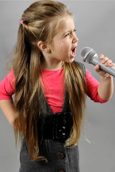 Malá dívka zpívá karaoke na šedém pozadí — Stockfoto