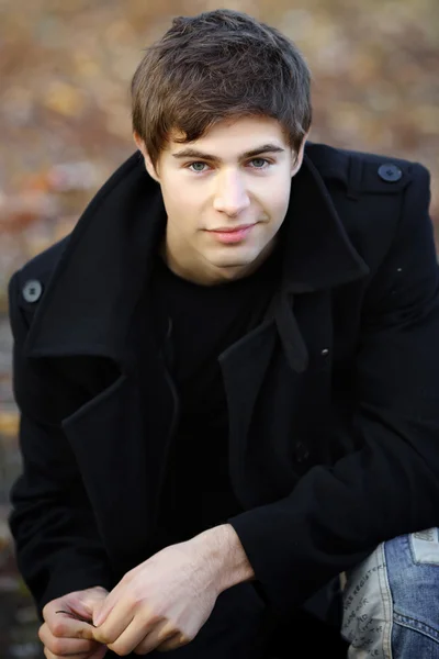 Πορτρέτο του ένας όμορφος νεαρός σε ένα μαύρο παλτό Φωτογραφία Αρχείου